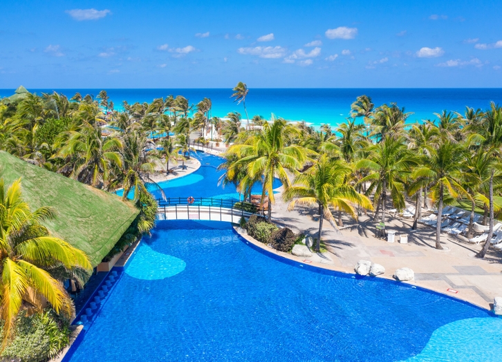 Tropical pool surrounded by palm trees overlooking the sea at Grand Oasis Cancun